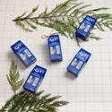 Dr. Bronners peppermint essential gift sets lay on a white tiled surface, surrounded by green pine branches. The packaging highlights Dr. Bronners eco friendly, vegan, organic soap products [One Size]