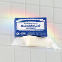 Dr. Bronners Magic Bar Soap, Peppermint, sits on a wet surface, creating suds against a tiled background with a faint rainbow. DR. BRONNERS ALL ONE PURE CASTILE MAGIC BAR SOAP PEPPERMINT. MADE WITH REGENERATIVE ORGANIC CERTIFIED OILS [5 oz]