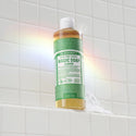 A bottle of Dr. Bronners eucalyptus castile soap stands on a white tiled shower ledge, with a soapy trail beneath it. A rainbow reflection appears on the tiles [16 oz]