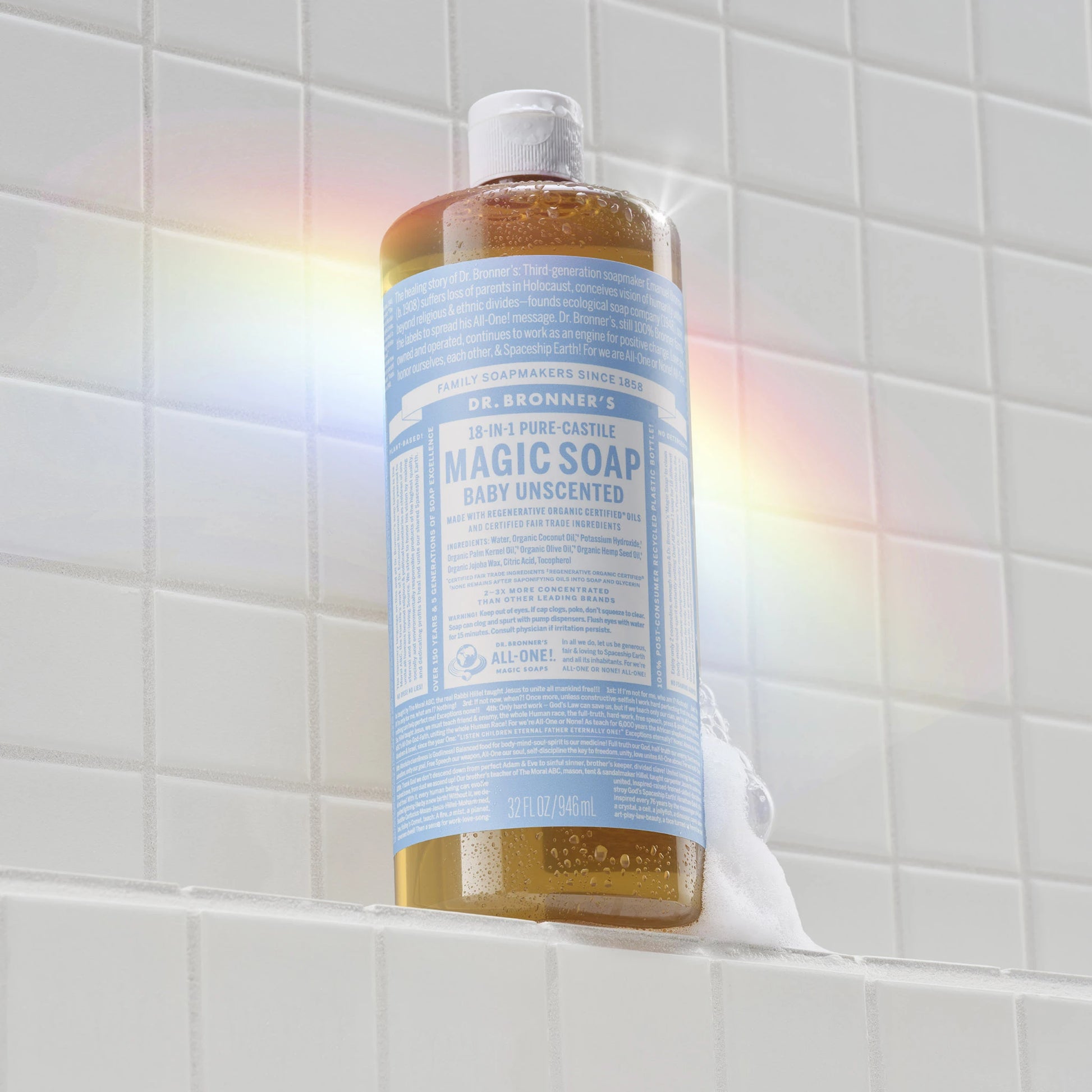 A bottle of Dr. Bronners Baby Unscented Pure Castile Liquid Soap stands vertically on a tiled surface, catching sunlight to create a subtle rainbow effect [32 oz]